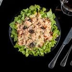 A delicious tuna salad with olives, lettuce, and fresh vegetables served on a black plate.