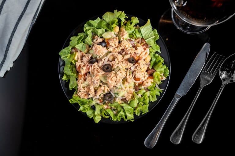 A delicious tuna salad with olives, lettuce, and fresh vegetables served on a black plate.