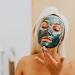 A woman applying a cosmetic face mask at home for skincare and relaxation.