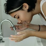 A woman with short hair gently washes her face at a bathroom sink, embracing a clean and refreshing start to the day.