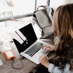 A young woman works remotely at a café, using her laptop and external hard drive.
