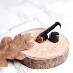Close-up of lip balm on a wooden slice against a marble background, featuring a dried leaf.