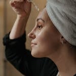 Close-up side view of a woman applying skincare serum with a dropper, promoting beauty routine.