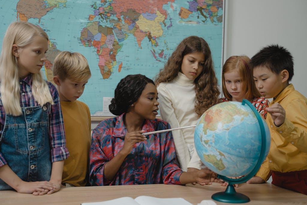 elementary students learning geography with a teacher and globe in the classroom getting ready to give her a gift for teacher appreciation week.