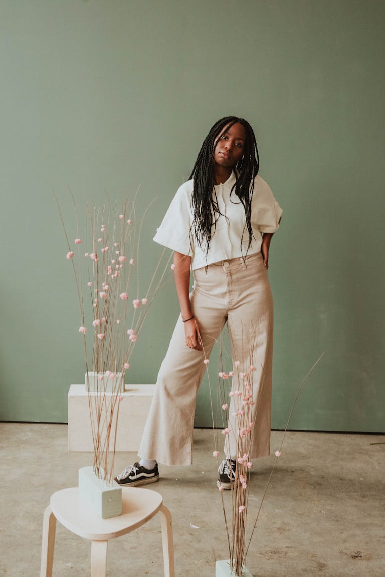 Full body of young African American female with long braids in trendy outfit standing in creative studio with closed eyes