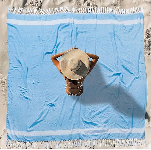 oversized beach towel in blue with a lady sitting on it in a hat