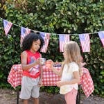 Kids enjoy a 4th of July celebration with drinks and American flags outdoors.