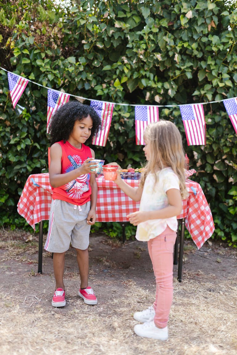 Kids enjoy a 4th of July celebration with drinks and American flags outdoors.