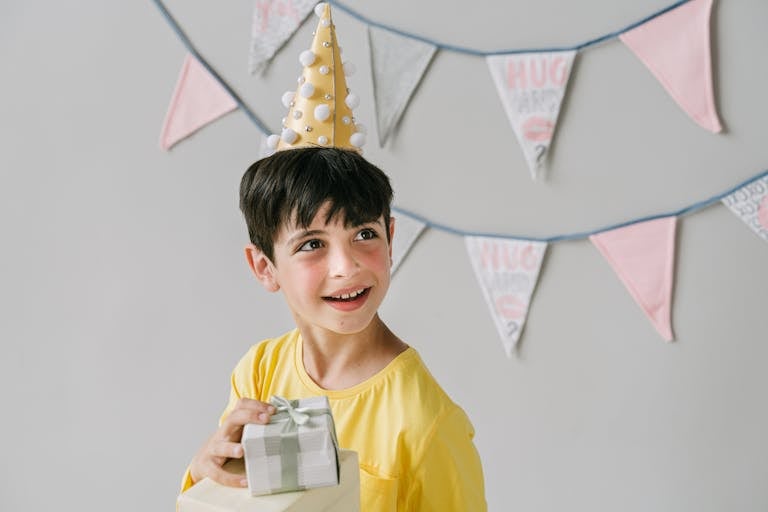 Young boy wearing party hat and holding a gift, celebrating birthday indoors.