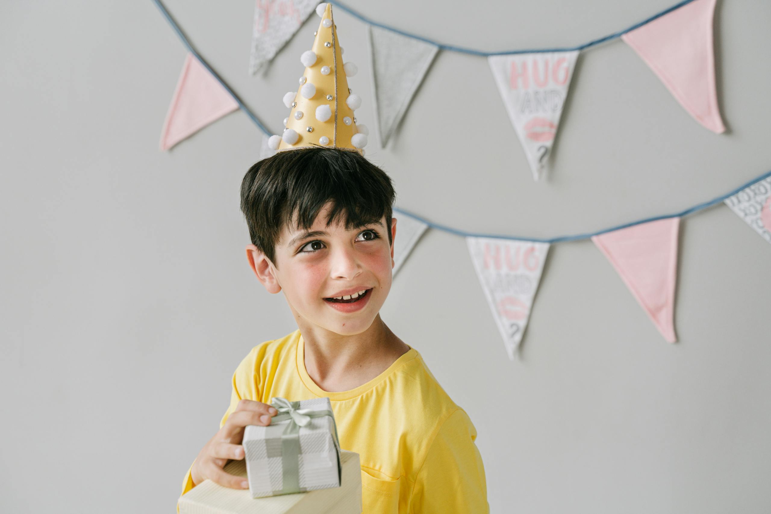 Young boy wearing party hat and holding a gift, celebrating birthday indoors.