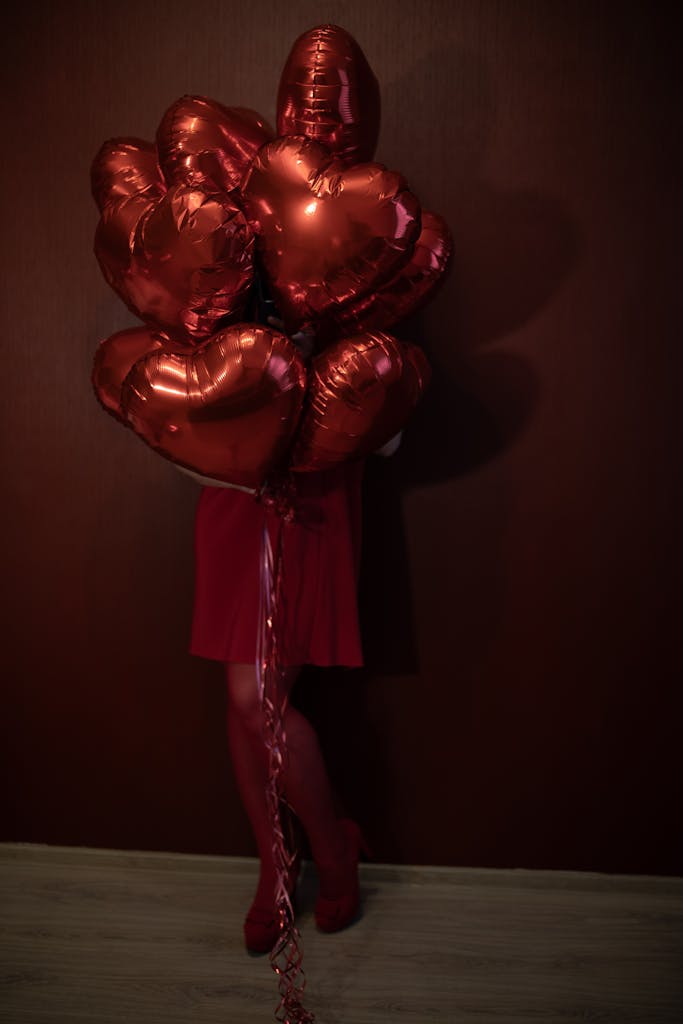 A woman in red holding heart-shaped balloons against a dark red background, symbolizing Valentine's Day.