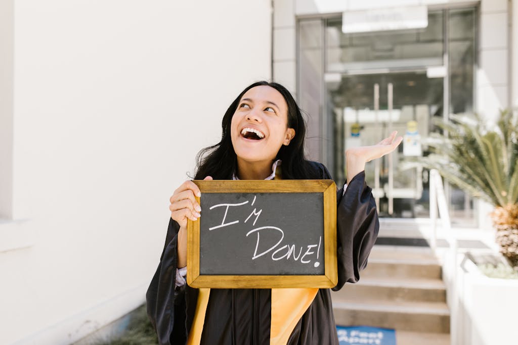 Happy graduate holding 'I'm Done!' sign outside a building, celebrating success.