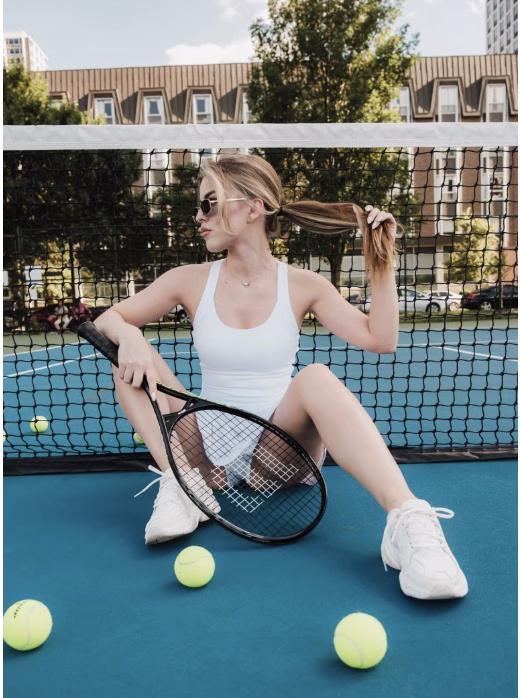 woman sitting on a tennis court with a racket and balls in front of her