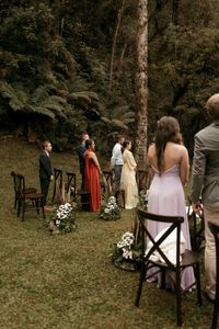 Elegant outdoor wedding ceremony with guests standing in a picturesque woodland setting.