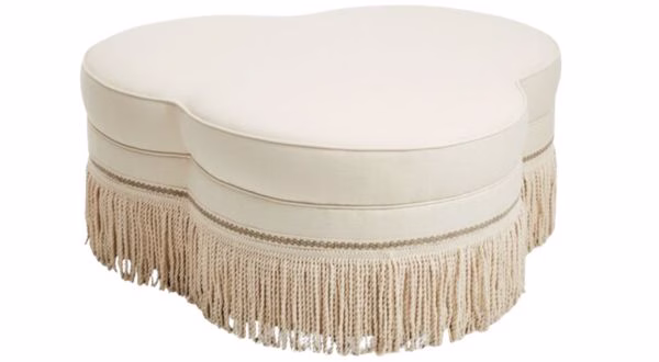 white oddly shaped ottoman coffee table with fringe on the bottom