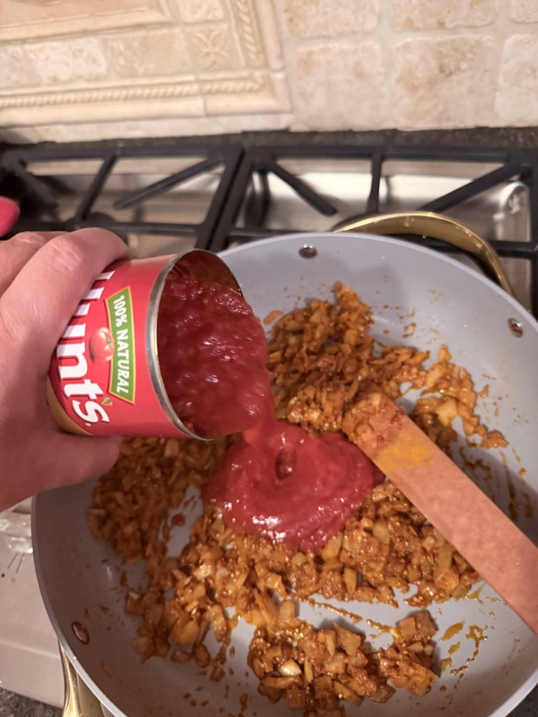 adding tomato sauce to simmering onions